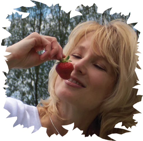 Candia Lea Cole smiling with closed eyes while holding a fresh ripe strawberry near her nose.